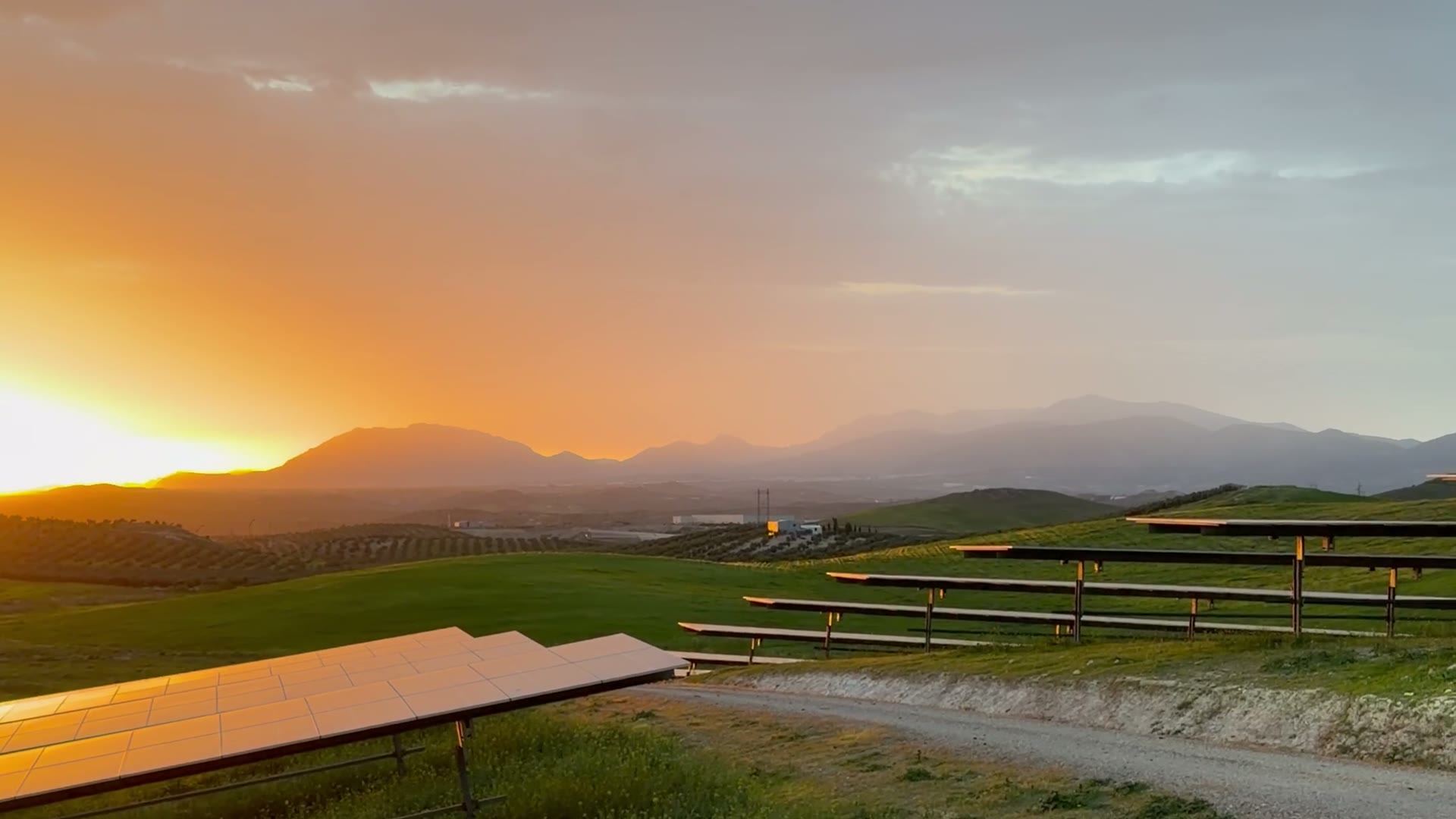Atardecer sobre filas de trackers de una planta fotovoltaica, con el sol tras las montañas