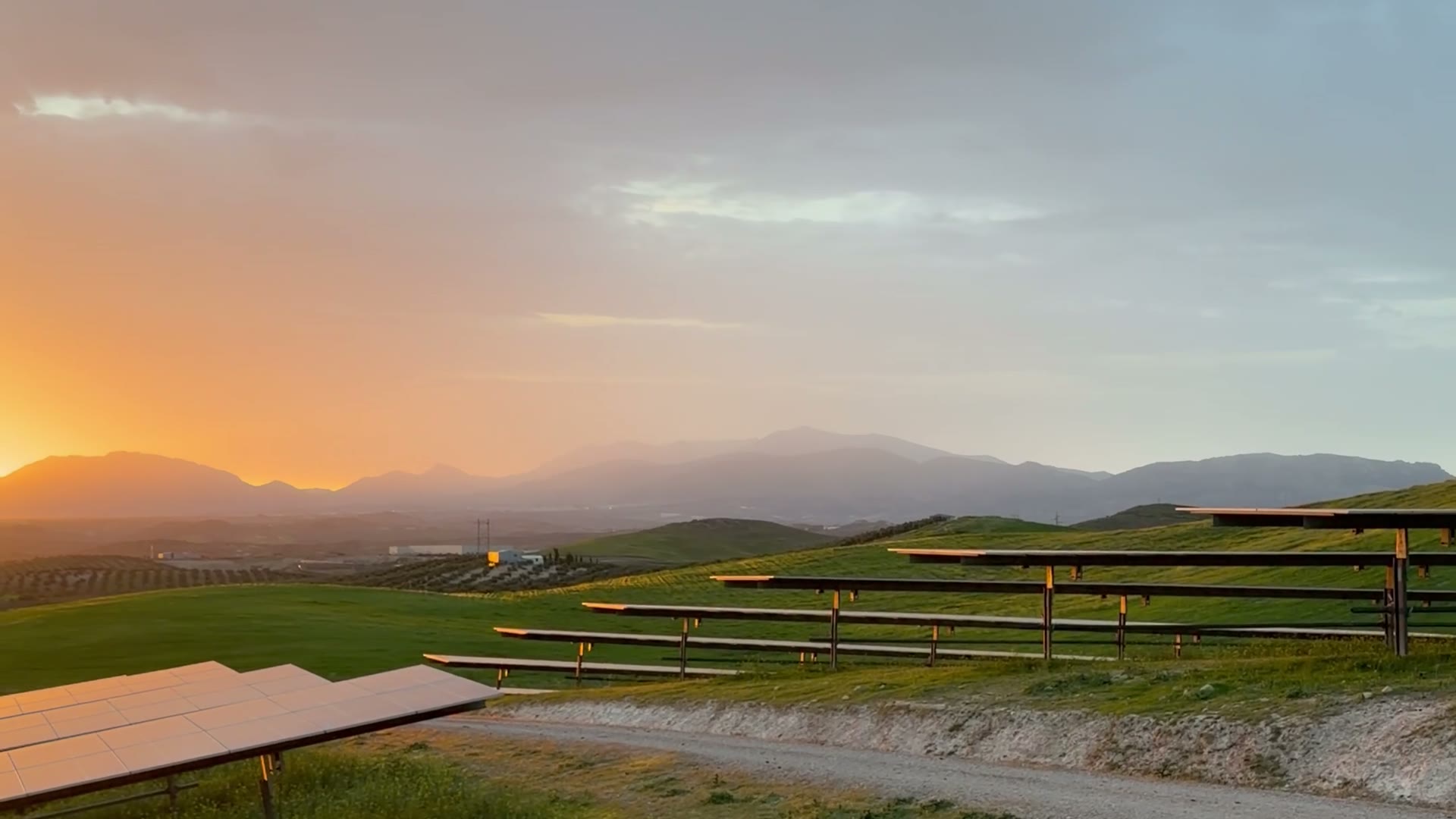 Filas de trackers a contraluz al atardecer, con montañas al fondo